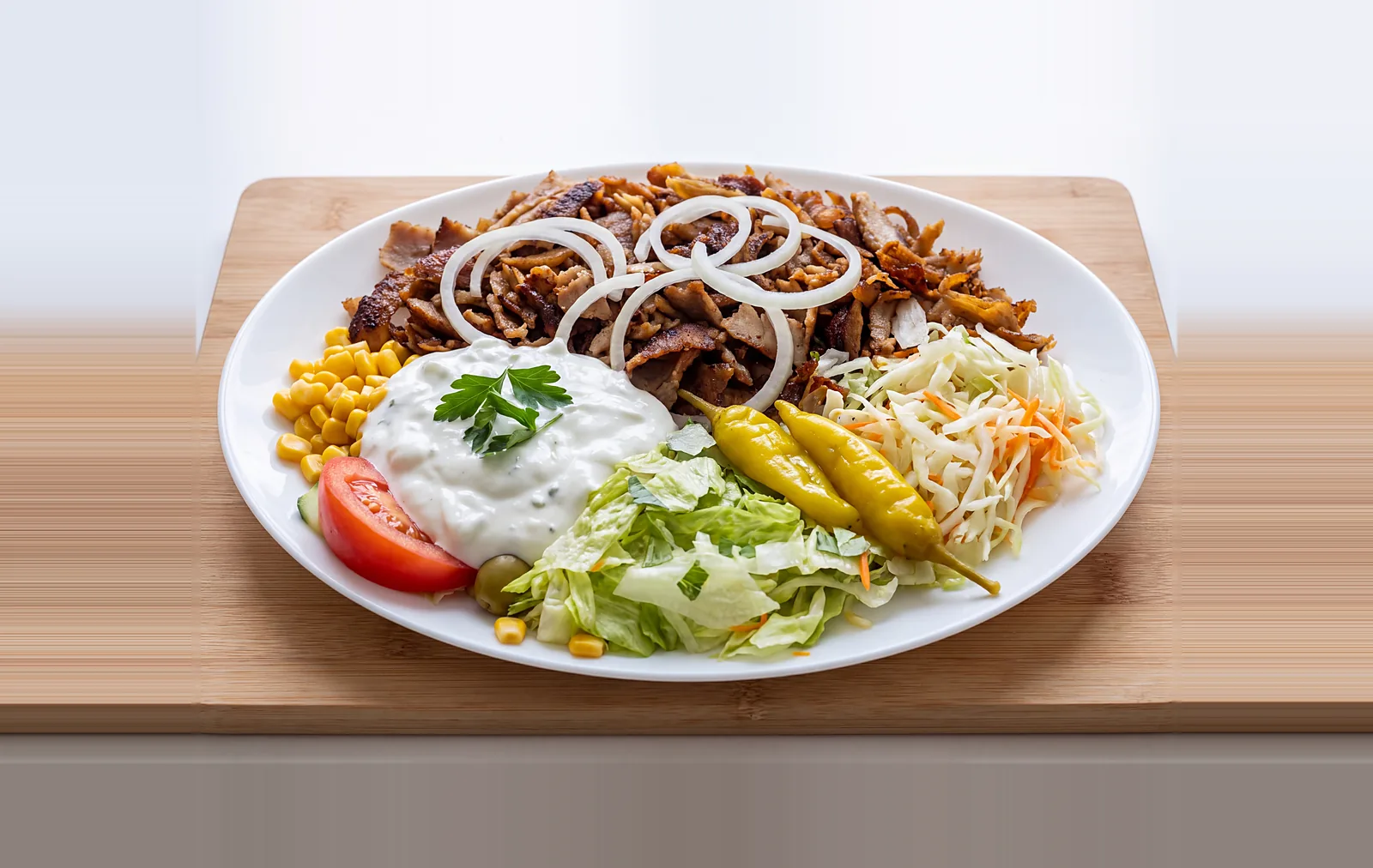 Gyros Teller mit Zwiebeln, Zaziki, Krautsalat, Peperoni und Tomate auf dem Holzbrett